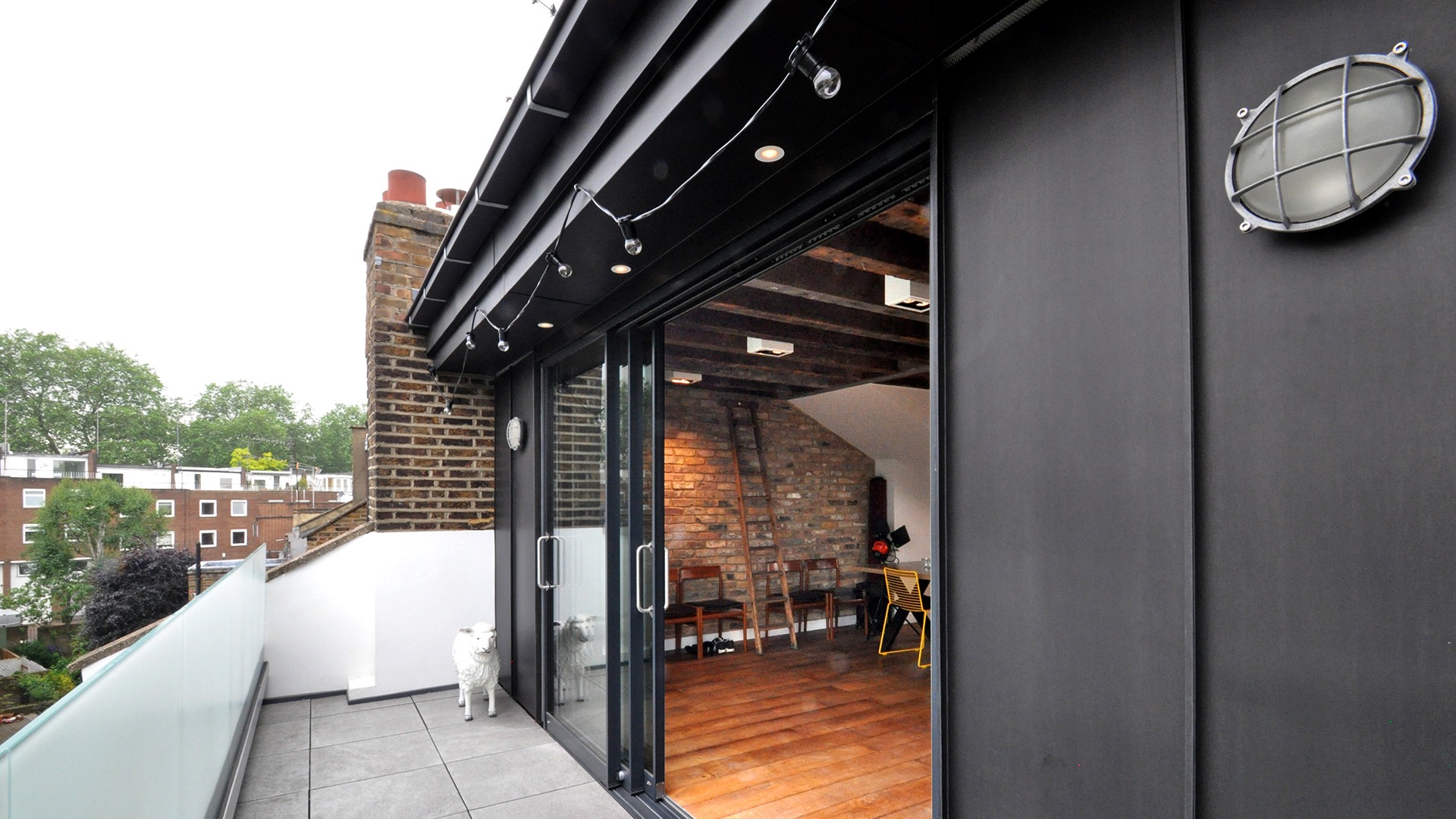Roof extension of Victorian terrace by a conservation architect to create a new kitchen living dining room for the property, with the creation of a roof terrace, porcelain tiles, obscure glazed balustrade, full height glazed sliding doors, black zinc cladding, inset spot lighting within soffit to parapet with integrated zinc box section gutter, repaired and restored brickwork, reclaimed timber flooring and exposed joists to the roof, with box surface mounted downlights